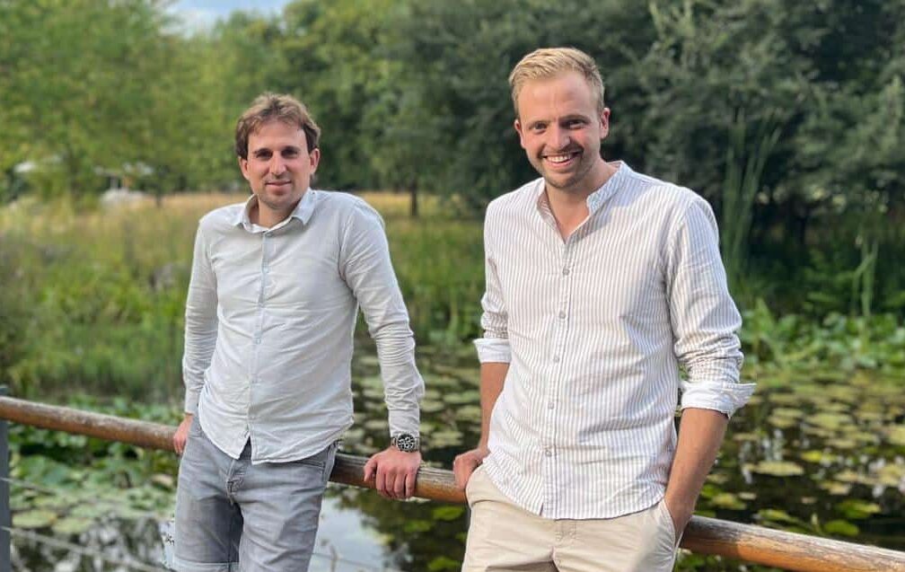 Nick und Nico stehen im Park an einer Brüstung, Darstellung des Teams von Nick & Nico Immobilien